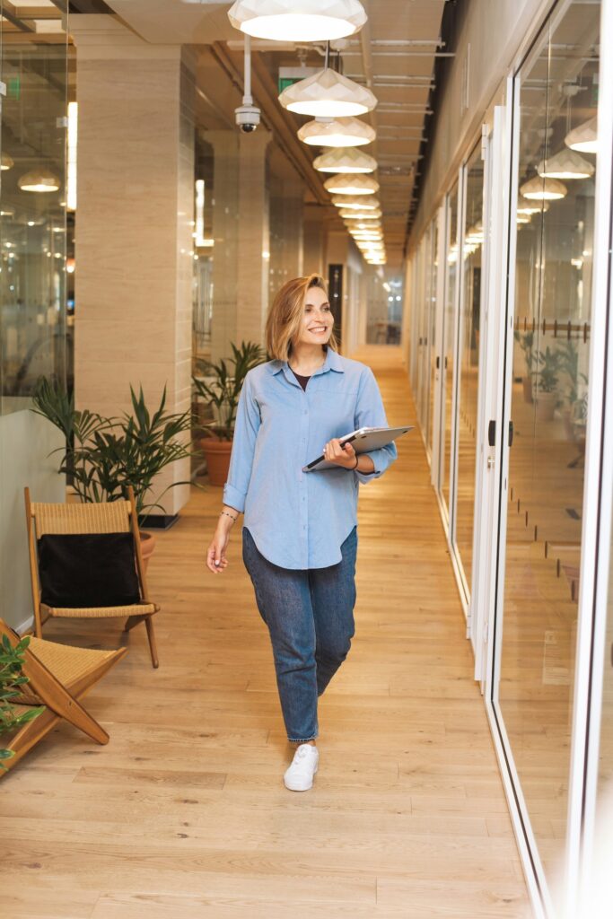 A woman smiling and walking in an office hallway holding a laptop.