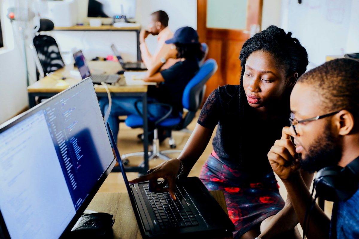 A man and woman sitting at a desk looking at a laptop.