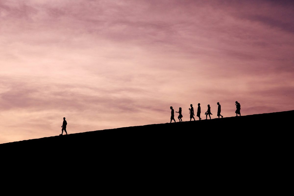 Silhouette of a group of people walking down a hill.